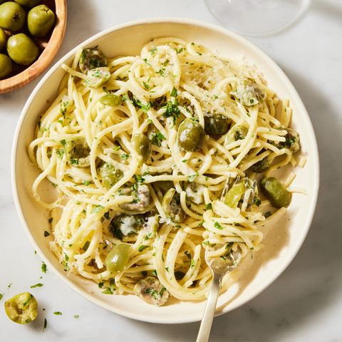 a bowl of spaghetti in a cream sauce with pieces of green olives, chopped parsley, and parmesan