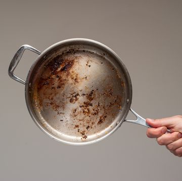 dirty oily burnt metal frying pan held in hand by male hand
