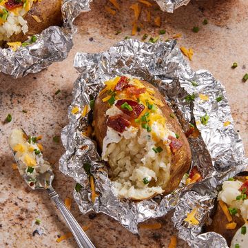 grilled baked potatoes in foil topped with sour cream, bacon, chives, and cheese