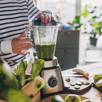 healthy eating, cooking, vegetarian food, dieting and people concept close up of young woman with blender and green vegetables making detox shake or smoothie at home